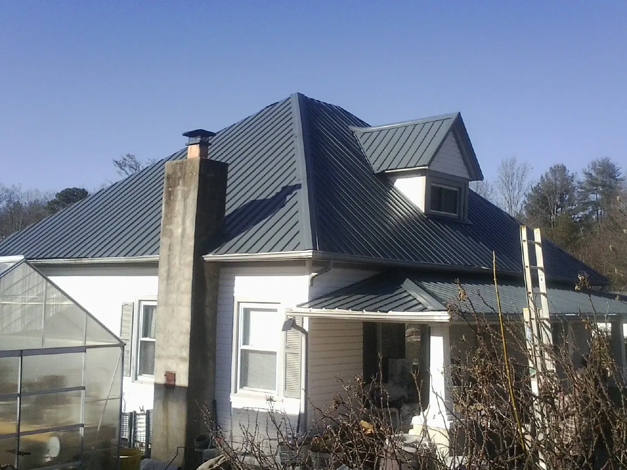 Dark blue standing seam metal roof on a white farmhouse with dormer — Slate & Tile Roof Repair by Roofing Brothers in Lake City