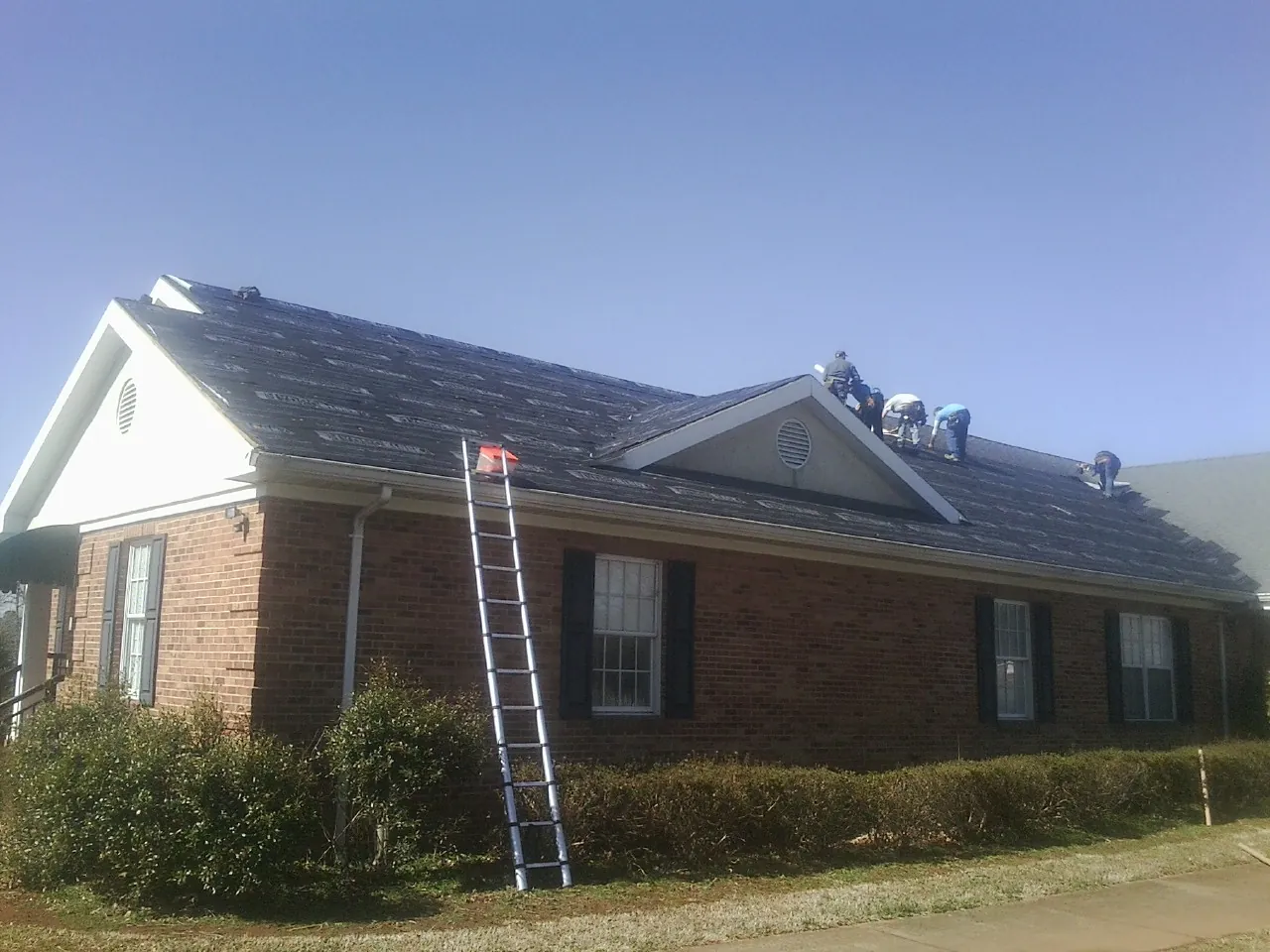 Crew tearing shingles off a brick ranch roof with a ladder set — Metal Roof Repair work by our crew in Lake City
