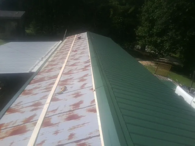 Old rusted panels beside newly installed green metal roofing — Wind Damage Roof Repair by Roofing Brothers in Lake City