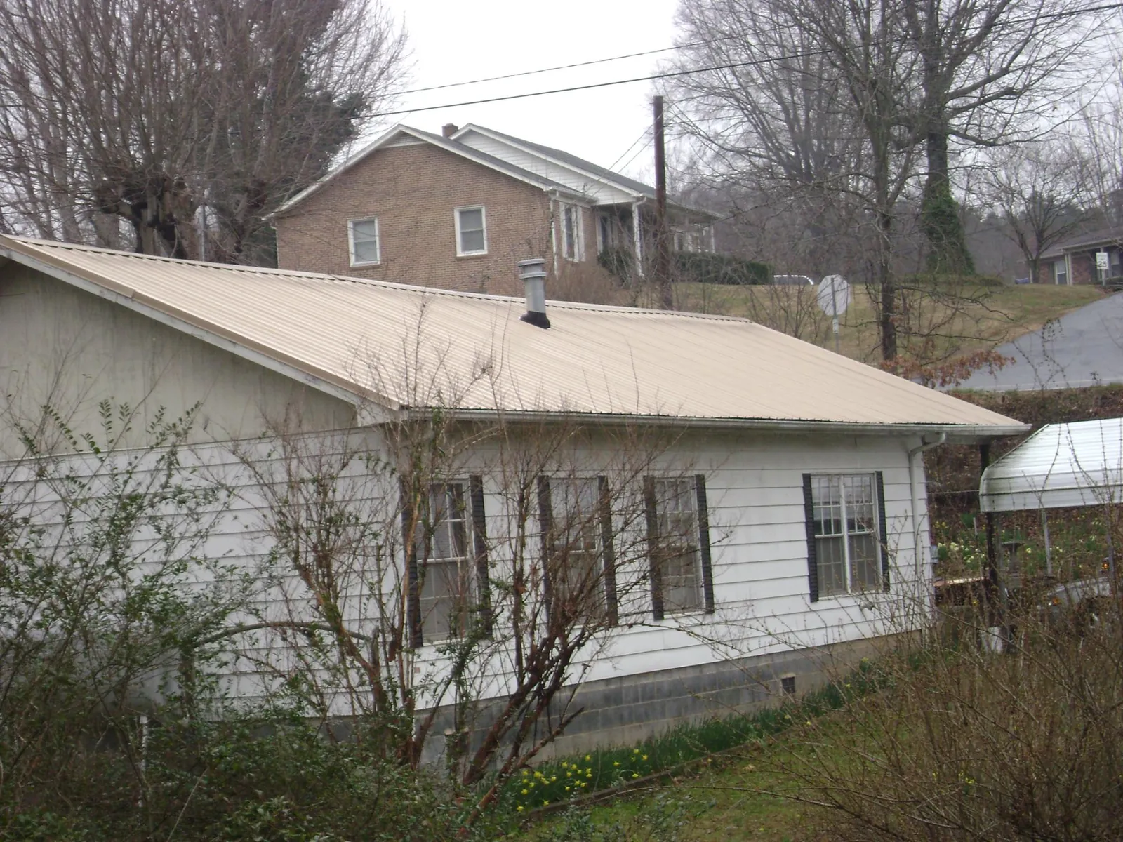 Tan metal roof on a white sided house set into a hillside — Commercial Roofing by Roofing Brothers in Lake City